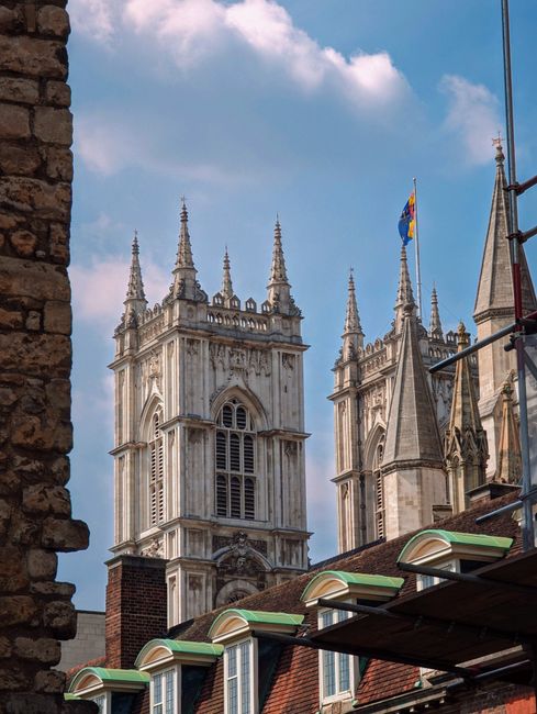 An exterior view of Westminster Abbey showcasing its Gothic architecture with intricate stone carvings, tall spires, and large stained glass windows. The façade displays a combination of light and da
